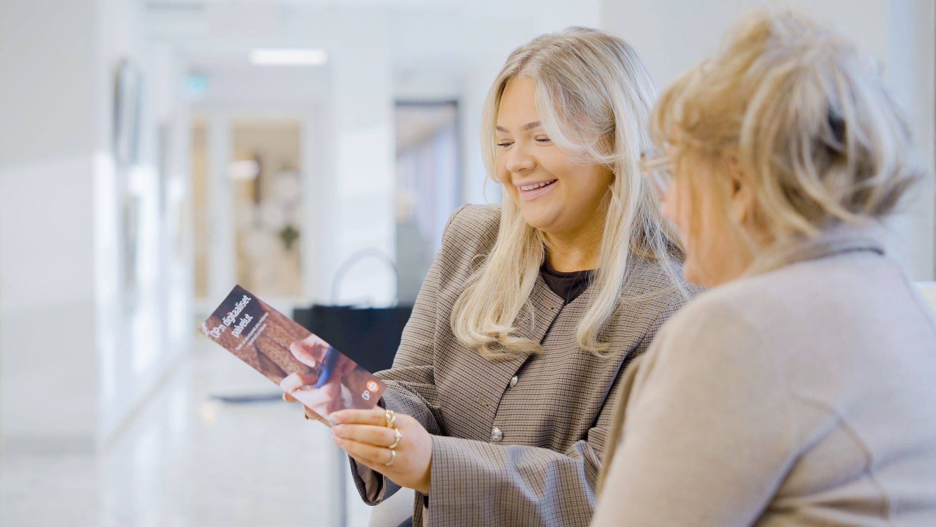 Digiopastuskuva, jossa pankkivirkailija opastaa pankkikonttorilla eläkeläisnaista.