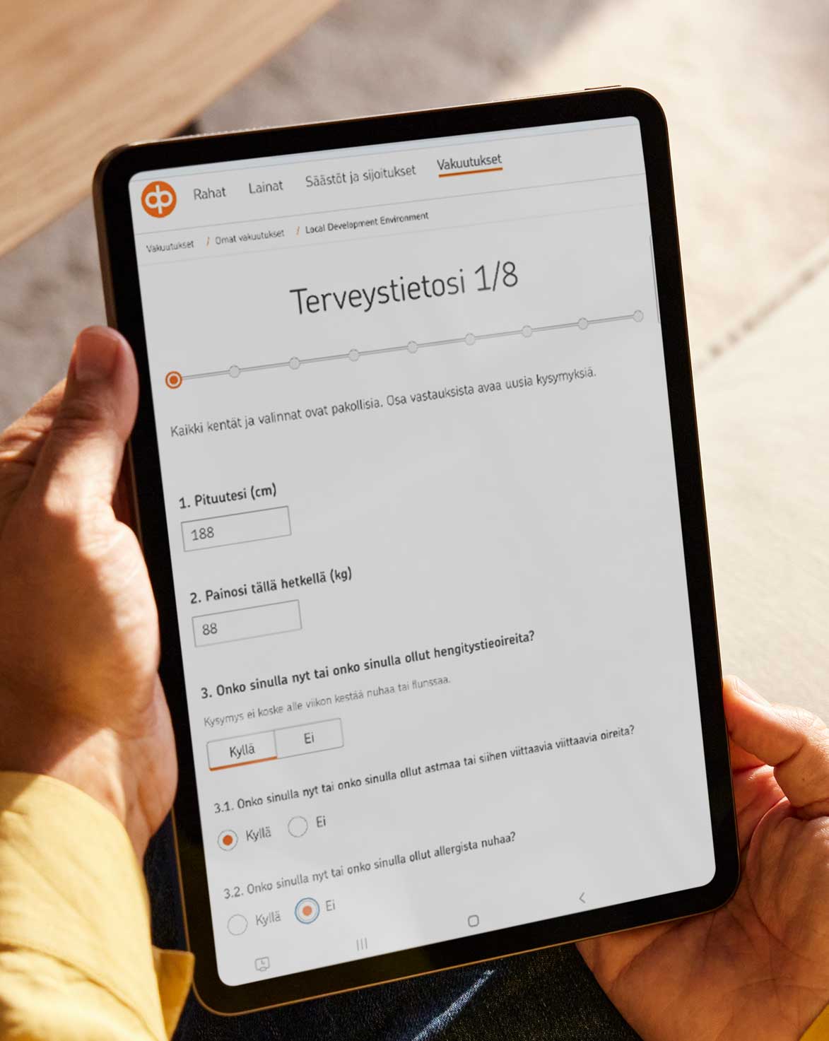 Tabletin näytöllä on terveysselvityslomakkeen ensimmäinen sivu, jossa viisi kysymystä näkyvillä.