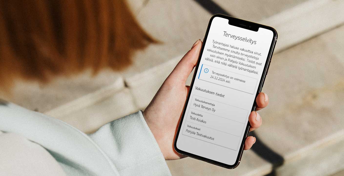 Punahiuksinen henkilö pitää vasemmassa kädessään puhelinta. Puhelimen näytöllä on terveysselvityksen ensimmäinen sivu.