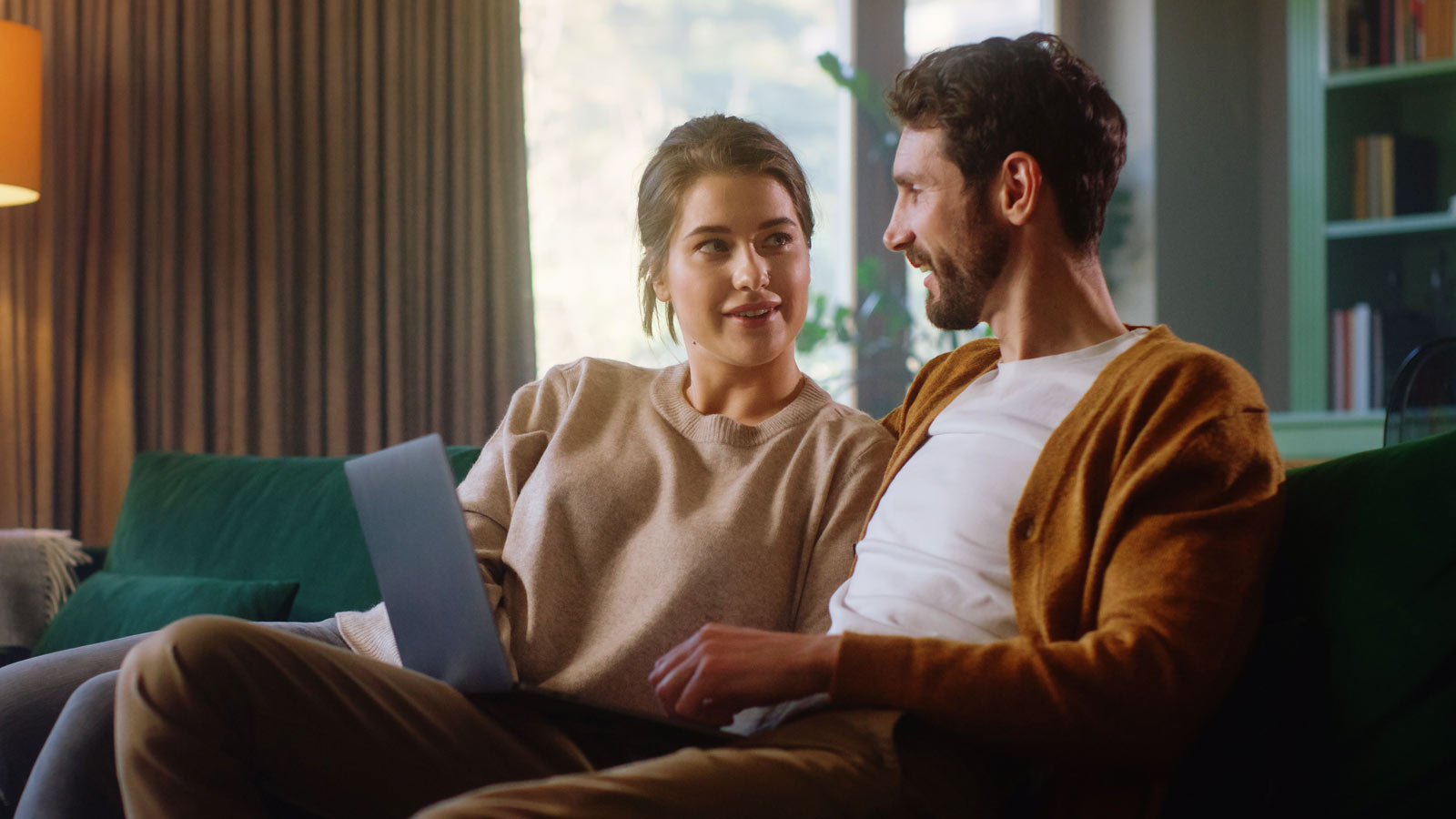 Pariskunta istuu sohvalla läppärin ääressä.