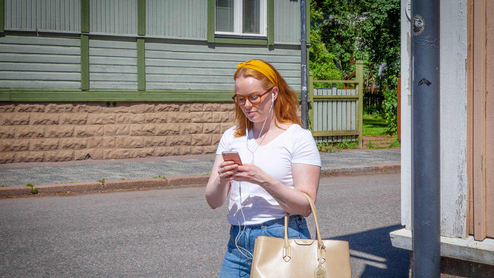 Nuori nainen katsoo puhelinta kuulokkeet korvilla.