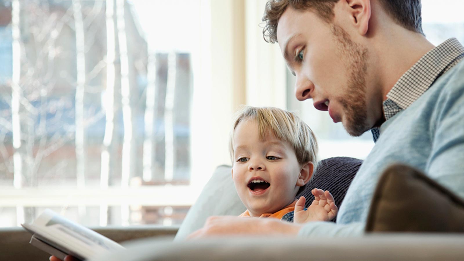 Isä lukee pojalle kirjaa sohvalla