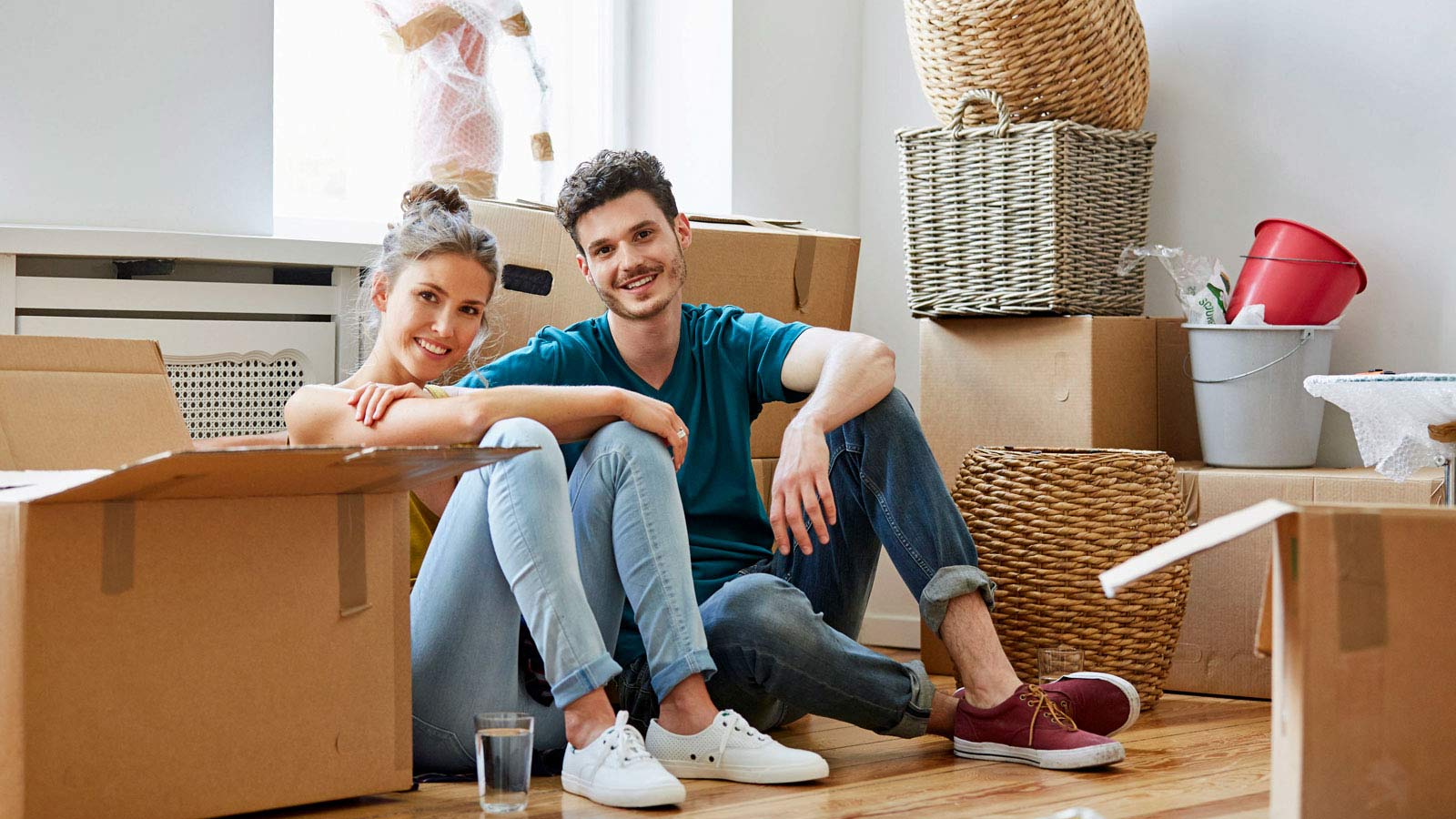 Nuori pariskunta istuu lattialla muuttolaatikoiden keskellä.