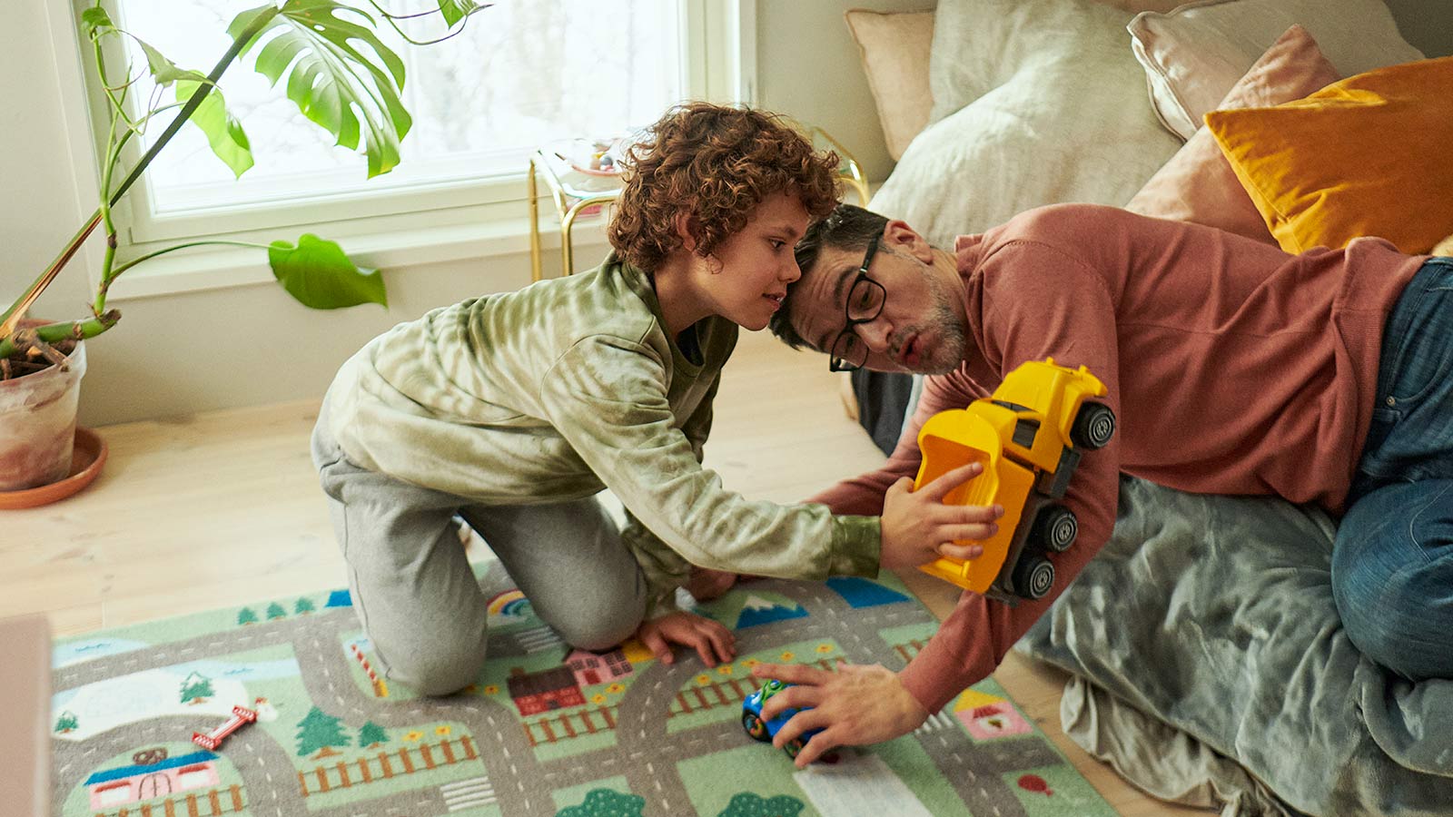 Lapsi ja aikuinen leikkivät lastenhuoneessa leluautoilla