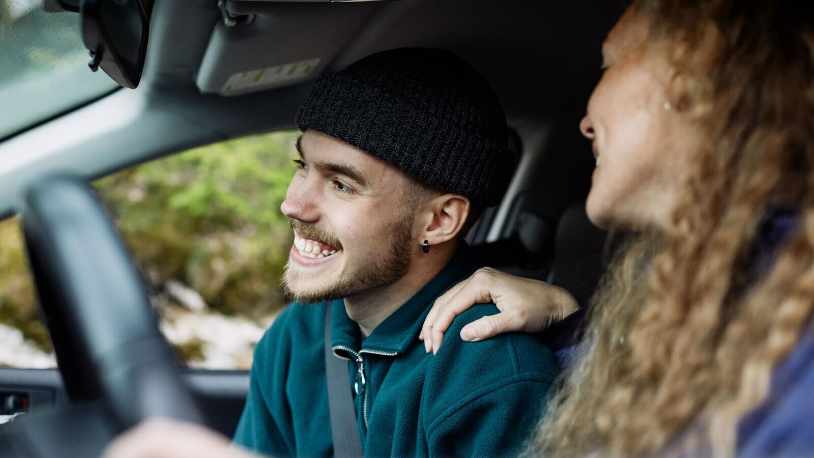 Kaksi ihmistä istuvat auton etupenkillä hymyillen