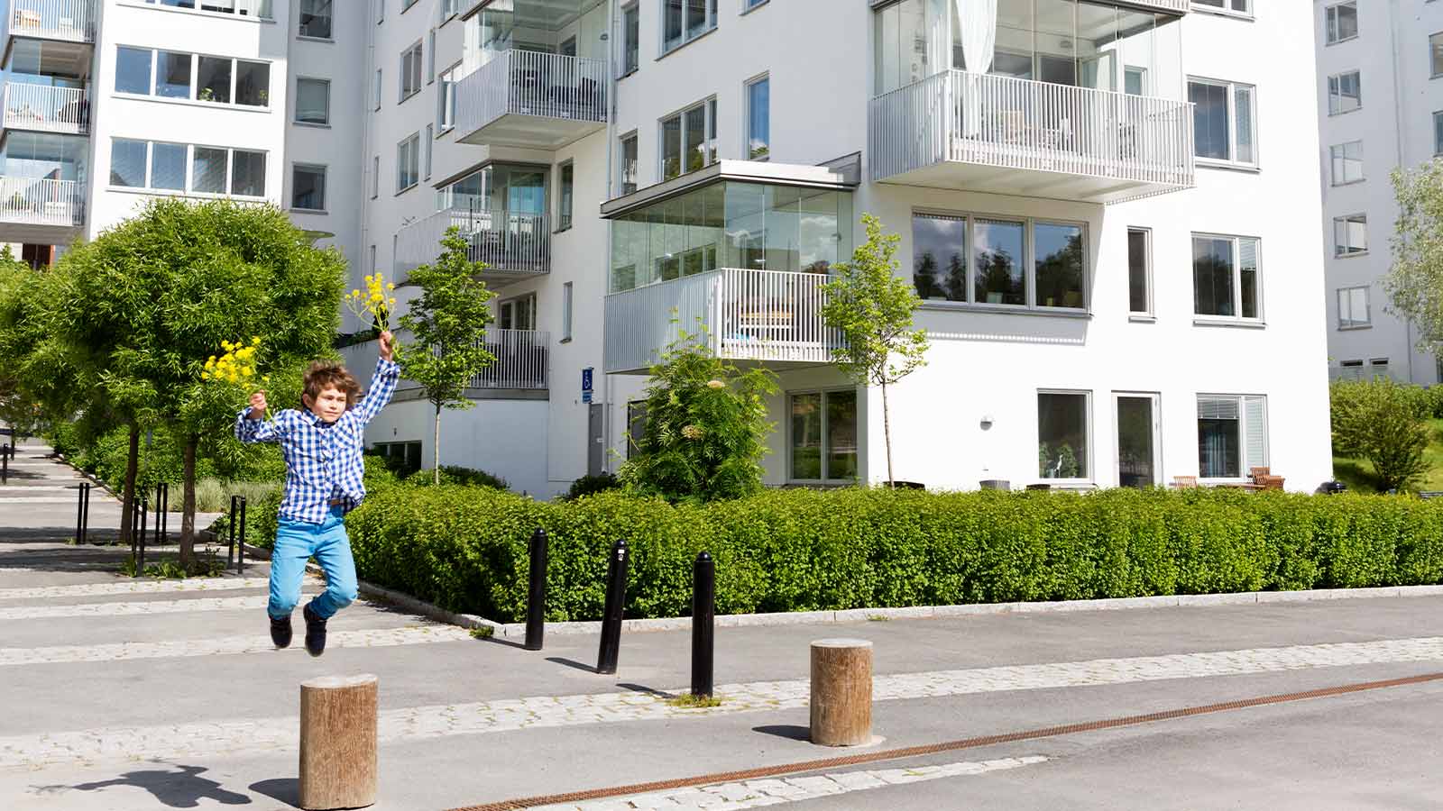 ”Sinipaitainen poika hyppii kadulla kukat käsissään uuden kotinsa pihassa,  jossa on taloyhtiön vakuutus”