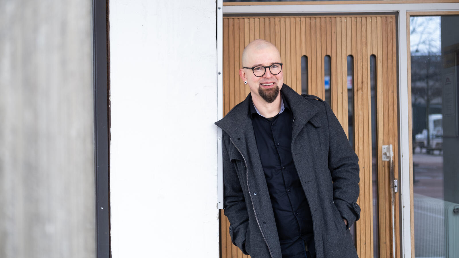 Hymyilevä mies nojaa talon ulkoseinään.