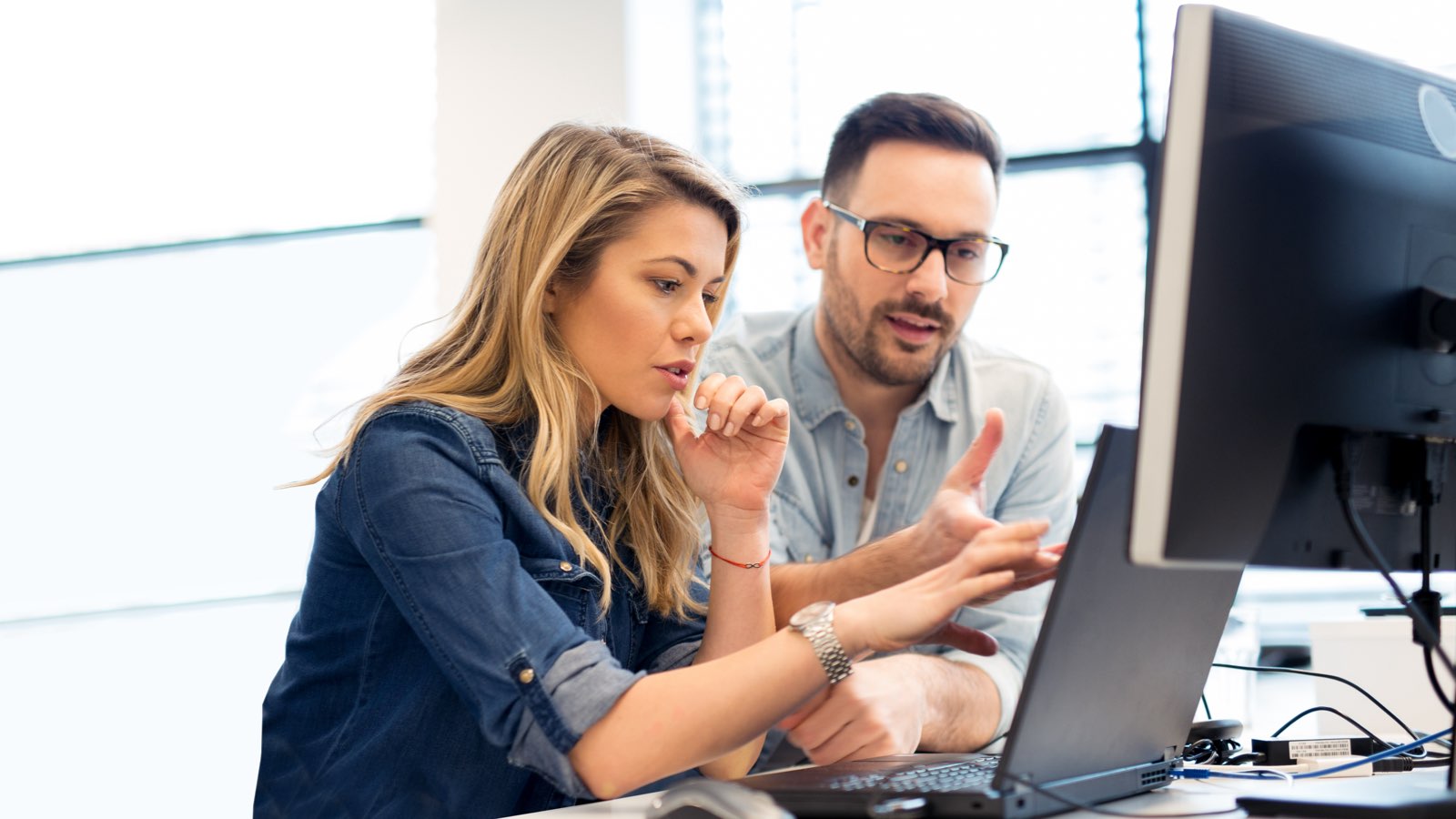 Mies ja nainen keskustelevat tietokoneen äärellä toimistossa.