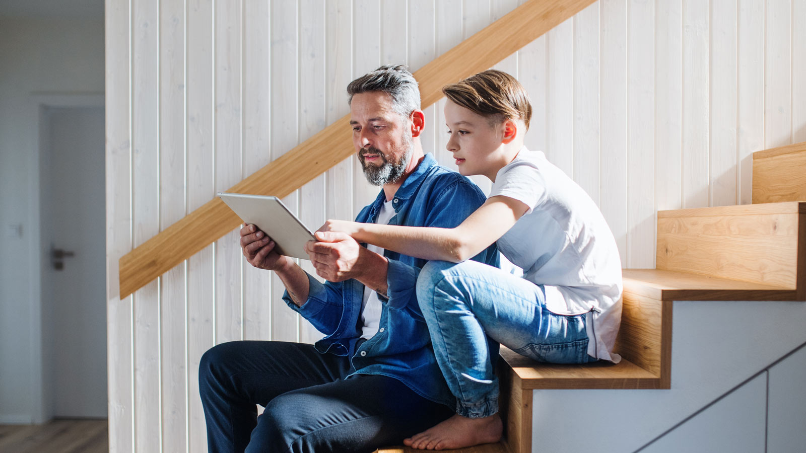Mies ja poika istuvat portailla ja katsovat tablettia
