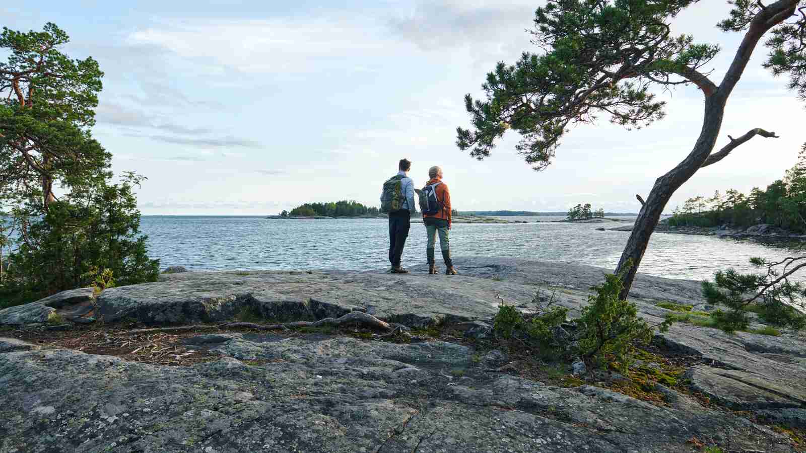 Kaksi retkeilijää katselevat rantakalliolla merelle kesällä.